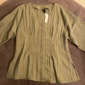 Grön blus - En fin mossgrön blus med smådetaljer såsom knappar fram och en lite indragen midja fram samt bak. Helt ny och aldrig använd. Köpte trots fel storlek eftersom det bara fanns en kvar, men kom tyvärr aldrig till användning då den är stor för mig. 