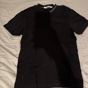 Svart t-shirt från Calvin Klein - Snygg svart t-shirt från Calvin Klein med klassisk design. Perfekt för en stilren look. T-shirten har korta ärmar och rund halsringning.