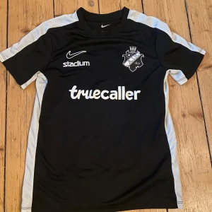 Svart AIK fotbollströja från Nike - Säljer en svart AIK fotbollströja från Nike med vit text och detaljer. Tröjan har korta ärmar och är tillverkad i Dri-FIT material för optimal komfort. Perfekt för AIK-fans! Passar folket som är mellan (11-13) år gamla. 