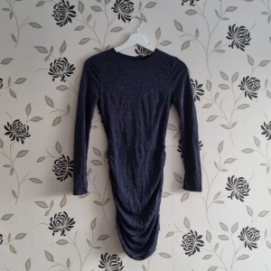 Mörkblå glittrig klänning, Nly Trend, Strl: XS/34, stretchig, - Snygg mörkblå klänning med glittrande detaljer och en öppen rygg. Klänningen har långa ärmar och en åtsittande passform som framhäver figuren. Perfekt för en kväll ute eller en speciell tillställning.