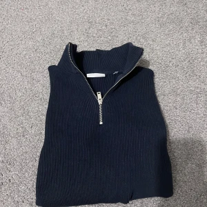 Svart ribbad tröja från Lindbergh - Snygg svart ribbad tröja från Lindbergh med dragkedja i halsen. Perfekt för en stilren look och passar bra till både vardag och mer uppklädda tillfällen.