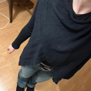 Svart poncho med knappar - Snygg svart poncho med dekorativa knappar på axlarna. Perfekt för lager-på-lager och ger en stilren look. Passar bra till jeans eller kjol för en avslappnad stil.