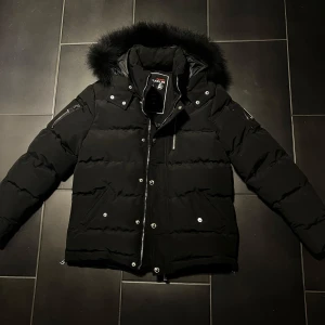 Svart dunjacka  Moose Knuckles - Jag säljer min nästan nya Moose Knuckles dunjacka som endast har använts en gång för att testa. Den är i utmärkt skick och ser  helt ny ut. Jackan är både varm och stilren, perfekt för kalla dagar. Den har en vattenavvisande yta och är fylld med högkvalitativ duntäcke för optimal komfort. Om du letar efter en pålitlig och snygg jacka, är detta ett utmärkt val!                                            Kontakta gärna innan köp.                                               Köpare står för frakt.