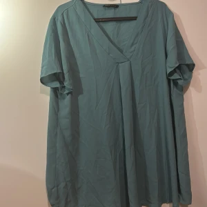 Blå blus med v-ringning - Snygg blå blus med v-ringning och korta ärmar. Perfekt för en avslappnad stil. Blusen har en lös passform och är tillverkad i ett lätt material.