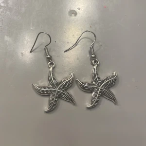 Silverfärgade sjöstjärneörhängen - hemma gjorda Snygga örhängen i form av sjöstjärnor med detaljerade prickmönster. De är silverfärgade och har en krok för enkel användning. Perfekta för att ge en marin touch till din stil. bra skick! håller jättebra.