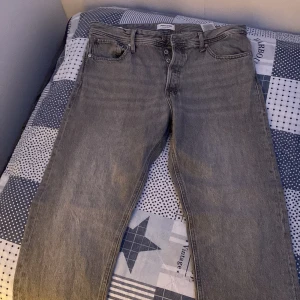 Jack jones Grå jeansbyxor - Snygga grå Jack Jones jeansbyxor med klassisk femficksdesign och knappgylf. Perfekta för en avslappnad stil. De har en rak passform och är tillverkade i slitstarkt denim. I nyskick