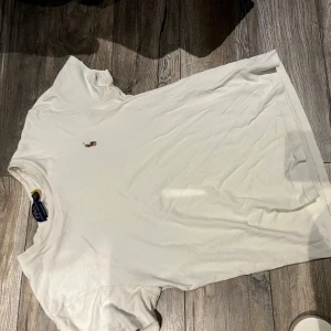 Vit t-shirt från Ralph Lauren - Säljer en klassisk vit t-shirt från Ralph Lauren med en liten broderad logga på bröstet. T-shirten har en normal passform och är tillverkad i mjukt bomullsmaterial. Perfekt för en stilren och avslappnad look.