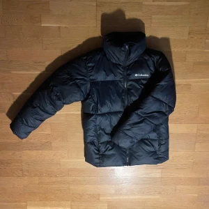 Svart pufferjacka från Columbia - Säljer en svart pufferjacka från Columbia i storlek S. Jackan är perfekt för kalla vinterdagar med sin tjocka vaddering och långa ärmar. Den har en hög krage och dragkedja framtill för extra värme. Perfekt för både vardag och utomhusaktiviteter! Storlek är s men passar som en m.