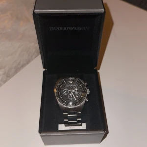 klocka från Emporio Armani - Säljer en stilren och elegant silverfärgad klocka från Emporio Armani. Klockan har en detaljerad urtavla med flera små urtavlor och en robust metallarmband. Perfekt för både vardag och fest. Kommer med originalförpackning och äkthetsintyg. Finns även extra länkar.