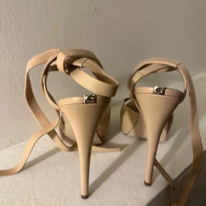 Beige klackskor från Guess - Säljer ett par eleganta beige klackskor från Guess i mycket bra skick. De har en snygg spetsig tå och knytband runt ankeln för extra stil. Perfekta för festliga tillfällen eller en utekväll. Klackarna är höga och ger en chic look.har använt dem till ett fest 
