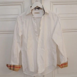 Vit skjorta från Burberry Brit - Säljer en stilren vit skjorta från Burberry Brit i storlek S. Skjortan har långa ärmar och klassiska Burberry-rutiga detaljer på insidan av kragen och ärmsluten. Perfekt för både vardag och fest! 🕺