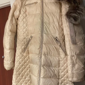Beige dunjacka från Rockandblue - Säljer en superfin beige dunjacka från Rockandblue i storlek 38. Kemtvättas inan vi skickar då den har lite fläckar. Jackan har en mysig pälskrage och quiltad design med dragkedjor. Perfekt för kalla vinterdagar! 🧥❄️