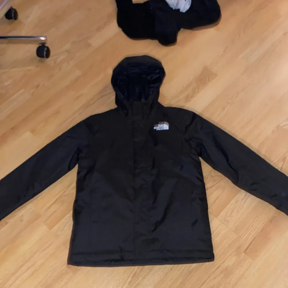 Säljer en svart vindjacka från The North Face i mycket bra skick. Jackan har en praktisk huva och långa ärmar, perfekt för blåsiga dagar. Den är gjord i ett slitstarkt material och har en diskret logga på bröstet. Perfekt för höst och vår! 12 år. Takit.