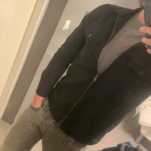 Svart jacka från Riley - Säljer en stilren svart jacka från Riley i storlek 46. Jackan har en dragkedja framtill och två bröstfickor med knappar. Perfekt för höst och vår, med en klassisk look som funkar till det mesta. Passar både till vardags och lite finare tillfällen.
