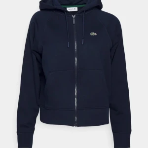 Mörkblå hoodie från Lacoste - Säljer en snygg mörkblå hoodie från Lacoste i mycket bra skick. Den har dragkedja och den klassiska krokodilloggan på bröstet. Perfekt för höst vinter vår. Strlk M jag är 172 o väger 63kg. Kp för frågor