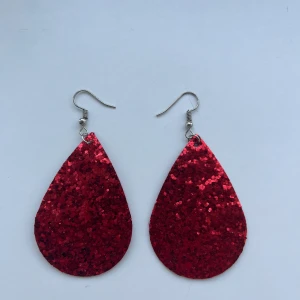 Röda glittriga örhängen - Snygga röda glittriga örhängen i droppform. Nickelfria krokar. Hämtas i Hornstull i Stockholm eller skickas mot fraktkostnad. ❤️