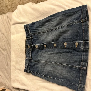 Jeanskjol med knappar - Säljer en snygg jeanskjol i bra skick. Den är kort och har en rad med knappar framtill som ger en cool look. Perfekt för både vardag och fest! 🥳Har knappt använd