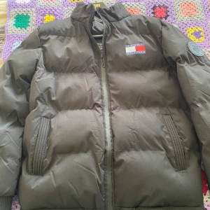 Svart dunjacka från Tommy Hilfiger - Säljer en svart dunjacka från Tommy Hilfiger i mycket bra skick. Jackan har en dragkedja framtill och ribbade muddar vid ärmsluten. Den är perfekt för kalla dagar och har en snygg logga på bröstet och ryggen. Passar både till vardags och lite finare tillfällen.