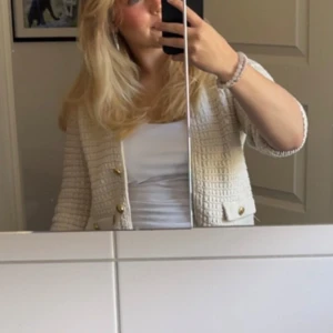 Vit stickad kofta med guldknappar - Säljer en superfin vit stickad kofta med guldknappar. Den har en elegant och klassisk stil med trekvartsärmar och två fickor fram. Perfekt för både vardag och fest!