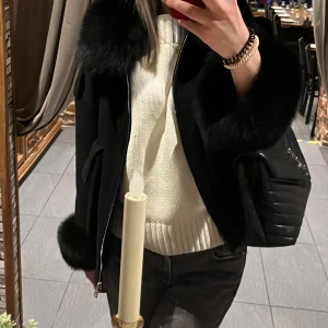 Svart jacka med pälsdetaljer, INTRESSEKOLL!!! - Säljer en snygg svart jacka med fluffiga pälsdetaljer på krage och ärmslut. Jackan har en dragkedja framtill och stora fickor. Pälsen är äkta och det är räv päls. Tyvärr har jackan gått sönder på två ställen men är lätt att fixa med nål och tråd😊 