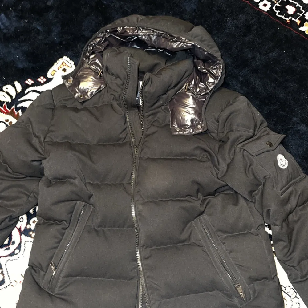 Säljer en snygg svart dunjacka från Moncler i mycket bra skick. Jackan har en quiltad design med dragkedja och en praktisk huva. Perfekt för kalla vinterdagar. Den har också en cool Moncler-logga på ärmen. Passar både till vardags och fest!. Jackor.