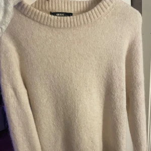 Beige stickad tröja från Bik Bok - Mysig beige stickad tröja från Bik Bok i mycket bra skick. Perfekt för höst och vinter med sin varma och mjuka känsla. Tröjan har långa ärmar och en ribbad rund halsringning samt ribbade muddar vid ärmslut och nederkant. Enkelt att matcha med jeans eller kjol för en avslappnad look.