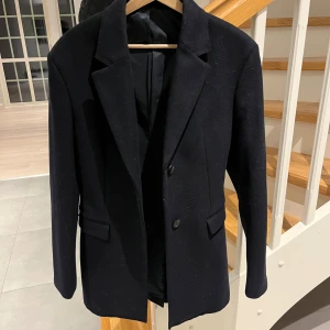 Kappa Filippa k  - Kortare Kappa från Filippa k i navy blue. Ullblanding som håller varmt under vintern. Använd några gånger bara så den ser ut som helt ny inga defekter alls. Hör av er vid frågor!