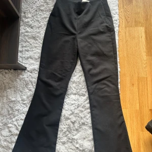 Svarta byxor från H&M - Snygga svarta byxor från H&M i storlek M. De har en hög midja och en bootcut-stil som ger en trendig look. Perfekta för både vardag och fest! Byxorna har en dragkedja på sidan för enkel på- och avtagning.