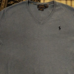 Blå v-ringad tröja från Polo Ralph Lauren - Säljer en stilren blå v-ringad tröja från Polo Ralph Lauren. Tröjan är i mycket bra skick och har en liten broderad logga på bröstet. Perfekt för både vardag och lite finare tillfällen. Passar bra till jeans eller chinos!