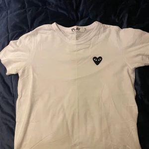 Vit t-shirt från Comme des Garçons - Säljer en stilren vit t-shirt från Comme des Garçons med det ikoniska svarta hjärtat med ögon på bröstet. Storleken är S, men skulle säga den är mer mot en xs! Skicket är mycket bra, hör av dig vid minsta fundering!😁