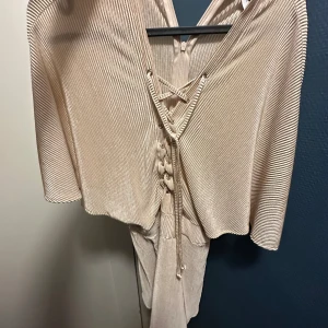 Beige ribbad klänning - Säljer en snygg beige ribbad klänning med knytning framtill. Den har en v-ringad design och trekvartsärmar, perfekt för både vår och sommar. Klänningen är i mycket bra skick och passar till både vardag och fest.