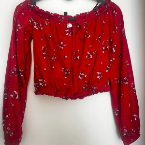 Röd blommig topp från H&M Divided - Säljer en superfin röd blommig topp från H&M Divided i storlek XS. Toppen har långa ärmar och en söt offshoulder-design med elastiska kanter. Perfekt för både vardag och fest! 🌸