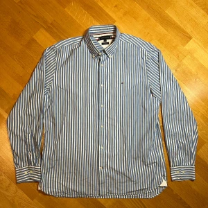 Vintage Blå och vit randig skjorta Tommy Hilfiger - Säljer en vintage blå och vit randig skjorta från Tommy Hilfiger i storlek XL. Skjortan har en normal passform och är långärmad med knappar framtill. Perfekt för både vardag och festliga tillfällen. Den är i mycket bra skick och redo för en ny ägare!