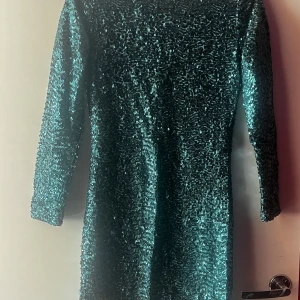 Grön glittrig klänning från Viced - Snygg grön klänning från H&M, perfekt för fest! Den är glittrig med paljetter och har en djup v-ringning. Klänningen har trekvartsärmar och är i mycket bra skick. Perfekt för att glänsa på nyår eller andra festliga tillfällen!