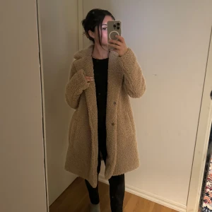 Beige teddyjacka - Mysig beige teddyjacka i mycket bra skick. Perfekt för höst och vinter med sin varma och gosiga stil. Jackan har långa ärmar och knappar framtill. Den är fodrad med ett mjukt material för extra komfort. Perfekt för att hålla sig varm och stilren under kyliga dagar! Precis som ny använt tre gånger. Original priset låg på 850