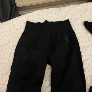 Svarta träningsshorts från Gymshark - Säljer ett par svarta träningsshorts från Gymshark i mycket bra skick. De är högmidjade och perfekta för gymmet eller löprundan. Materialet är stretchigt och bekvämt, vilket ger en tight passform. Perfekta för dig som vill ha stil och komfort under träningen!
