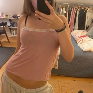 Rosa ribbat linne med spetsdetaljer - Säljer en söt rosa ribbad linne med vita spetsdetaljer längs kanten. 