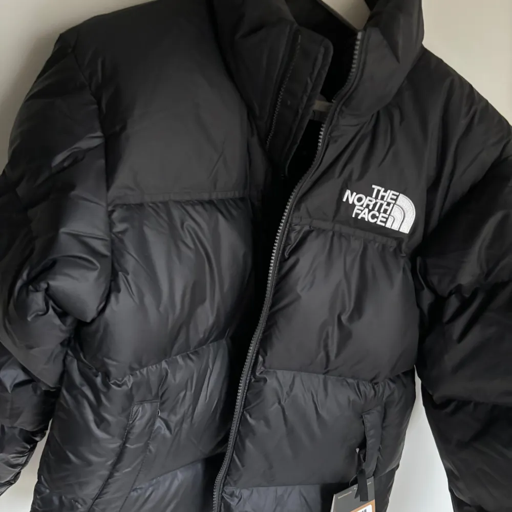 Säljer en svart pufferjacka från The North Face, helt nytt. Klassisk model 1996 Retro Nuptse Jacket. Jackan är perfekt för kalla vinterdagar med sin tjocka vaddering och långa ärmar. Den har en dragkedja framtill och loggan broderad på bröstet och ryggen. Superstylish och varm! 🖤Köpt från Paris i october, originalpris 350€. Jackor.