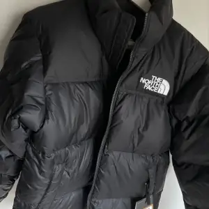 Säljer en svart pufferjacka från The North Face, helt nytt. Klassisk model 1996 Retro Nuptse Jacket. Jackan är perfekt för kalla vinterdagar med sin tjocka vaddering och långa ärmar. Den har en dragkedja framtill och loggan broderad på bröstet och ryggen. Superstylish och varm! 🖤Köpt från Paris i october, originalpris 350€