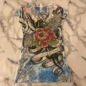 Säljer en unik och färgglad t-shirt med rhinestones, detaljer och mönster. T-shirten har korta ärmar och en v-ringad hals. Sitter tajt och snyggt! Storlek M men skulle säga att den är lite mindre i storleken! 🤍DM vid frågor osv!