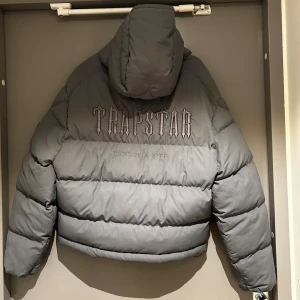 Trapstar jacket grey - Säljer en snygg grå pufferjacka från Trapstar i storlek S. Jackan har en cool broderad logga på ryggen och är perfekt för kalla dagar. Den är långärmad med dragkedja och har en skön huva. Perfekt för både höst och vinter! Inga tecken på andvändning, online kvitto finns, kan tänka mig diskutera priset bara höra av er :)