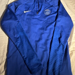 PSG Tracksuit. Tröjan för 550 och byxor på köpet !! - Säljer en blå långärmad träningströja från Nike med PSG-logga. Tröjan har en halv dragkedja och är i Dri-FIT material för bästa komfort under träning. Perfekt för fotboll eller annan sportaktivitet. Använd endast 6 gånger och i 9/10 skick. 2 för 1 !!!! 