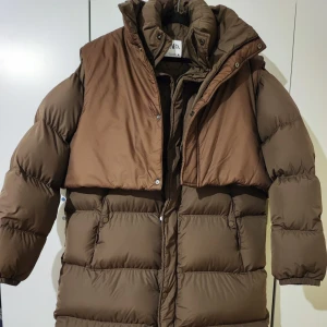 Brun lång dunjacka Zara x Adererror oversized puffer jacket - Säljer en supervarm och snygg brun lång dunjacka. Perfekt för kalla vinterdagar med sin pufferdesign och höga krage. Jackan har en cool, oversized och boxy look. Den är i mycket bra skick och redo för nya äventyr! The jacket is M size , will also perfectly for the L, it consists of 90% down, down's weight is 482 gr. Can send more real pictures! The coat is very stylish, amazing! Have minor signs of wear)