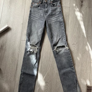 Grå jeans från Zara - Säljer ett par grå jeans från Zara i bra skick. De är hög/mellan midjade med slitna detaljer på knäna och slits nere vid fötterna. Perfekta för en casual look! Dock har ”örat” på sidan av midjan lossat lite grann men det är inget som syns. Säljer de för de är för små för mig. 