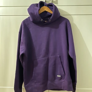 Lila hoodie med ficka - Säljer en snygg lila hoodie i mycket bra skick. Den har en stor ficka framtill och en justerbar huva med snören. Perfekt för höst och vinter när du vill hålla dig varm och bekväm. Passar både till vardags och chillkvällar. Köpt flera år sedan aldrig använt. Snören finns med men man måste installera dom själv. 🟣
