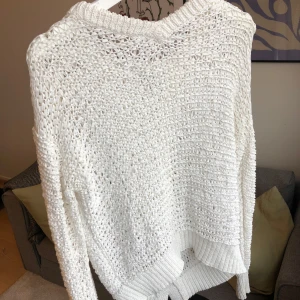 Vit stickad tröja från Dagmar, storlek S - Vit stickad tröja med ett fint mönster. Är lite lätt skimmer i tyget. Tröjan har en v-ringad halsringning och långa ärmar. Den är något längre med en ”skärning” baktill. Tröjan är i gott skick, men kan eventuellt skymta lite grånad vid halsringningen