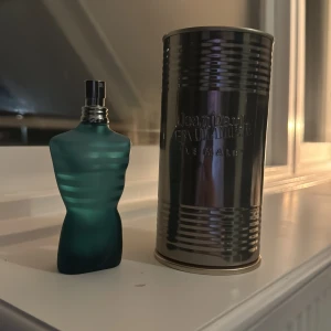 Jean Paul Gaultier ”LE MALÉ” - Säljer en cool parfym från Jean Paul Gaultier. Flaskan är formad som en manlig torso i en snygg blågrön färg med horisontella ränder. Den kommer med en metallisk förpackning som ger en industriell känsla. Perfekt för den som vill ha en unik och stilren parfymflaska på hyllan! (OBS PARFYMEN ÄR LITE ANVÄND)