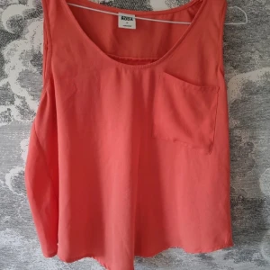 Linne från Vero Moda - Snygg korallfärgad ärmlös topp från Vero Moda. Toppen är i 100% polyester och har en cool omlottdetalj på baksidan. Den har en liten bröstficka och är i mycket bra skick.