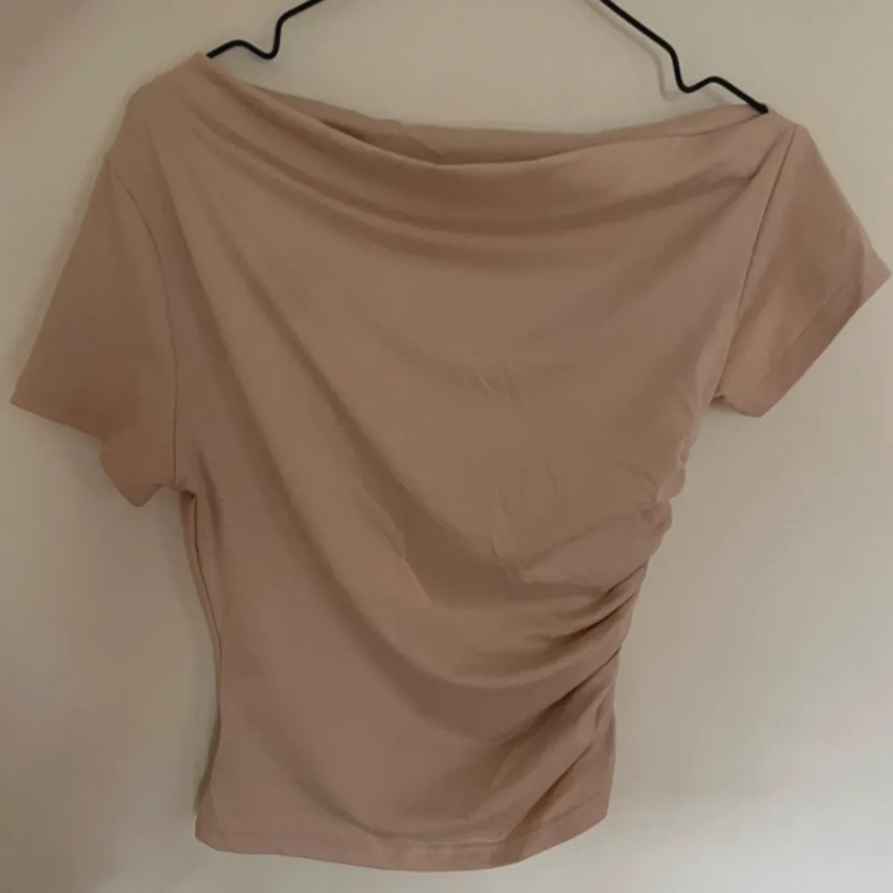 Säljer en snygg beige offshoulder topp med korta ärmar. Toppen har en cool rynkad detalj på sidan som ger den en unik look. . Toppar.