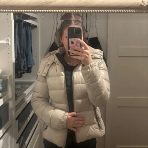 Beige/vit glansig  pufferjacka med huva - Säljer en supermysig beige pufferjacka med huva. Jackan har dragkedja och är perfekt för kyliga dagar. Den är i bra skick och passar perfekt för höst och vinter. Jackan har nypris 3000 ungefär.Storleken är dam S och den har en normal passform. Perfekt för att hålla sig varm och snygg! 🧥✨